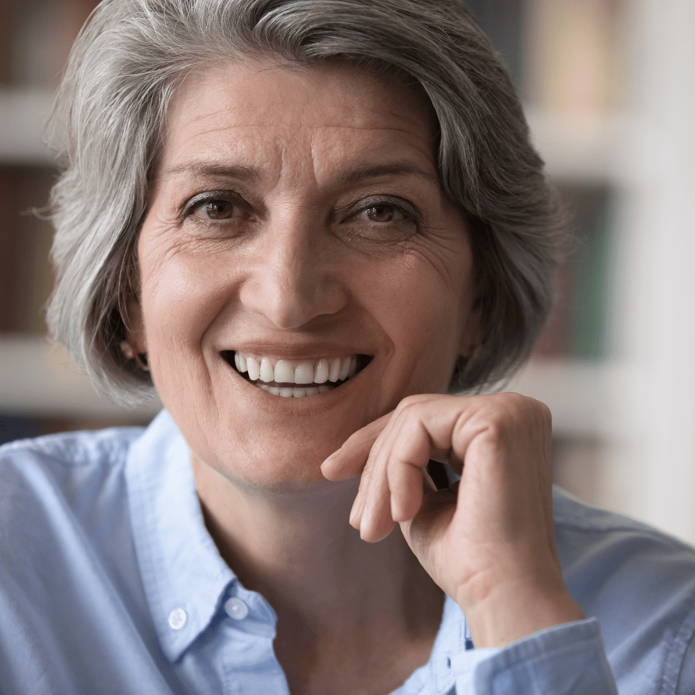 Mulher 58+ sorridente, com a mão no queixo, feliz da vida.