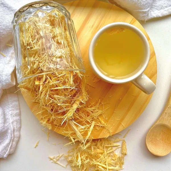 Xícara branca com chá de Molungu pronto para consumo, acompanhada de vidro com a planta triturada in natura solta, em cenário acolhedor.